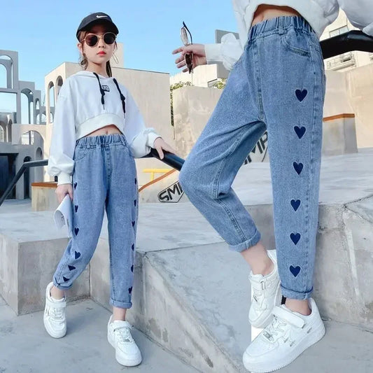 Two people wearing light blue jeans with heart patterns, standing on a concrete surface.