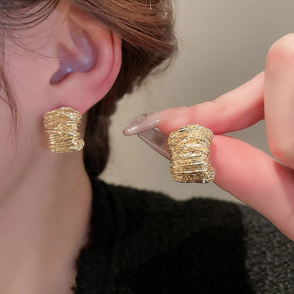 Gold textured earrings being worn and held up to the ear.