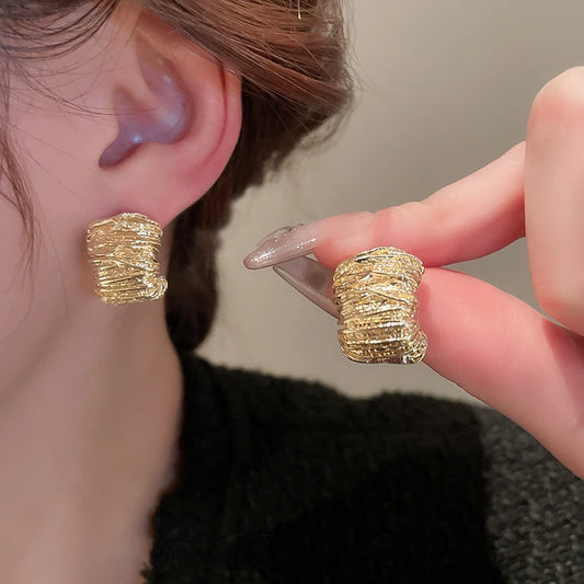 Gold textured earrings being worn and held up to the ear.